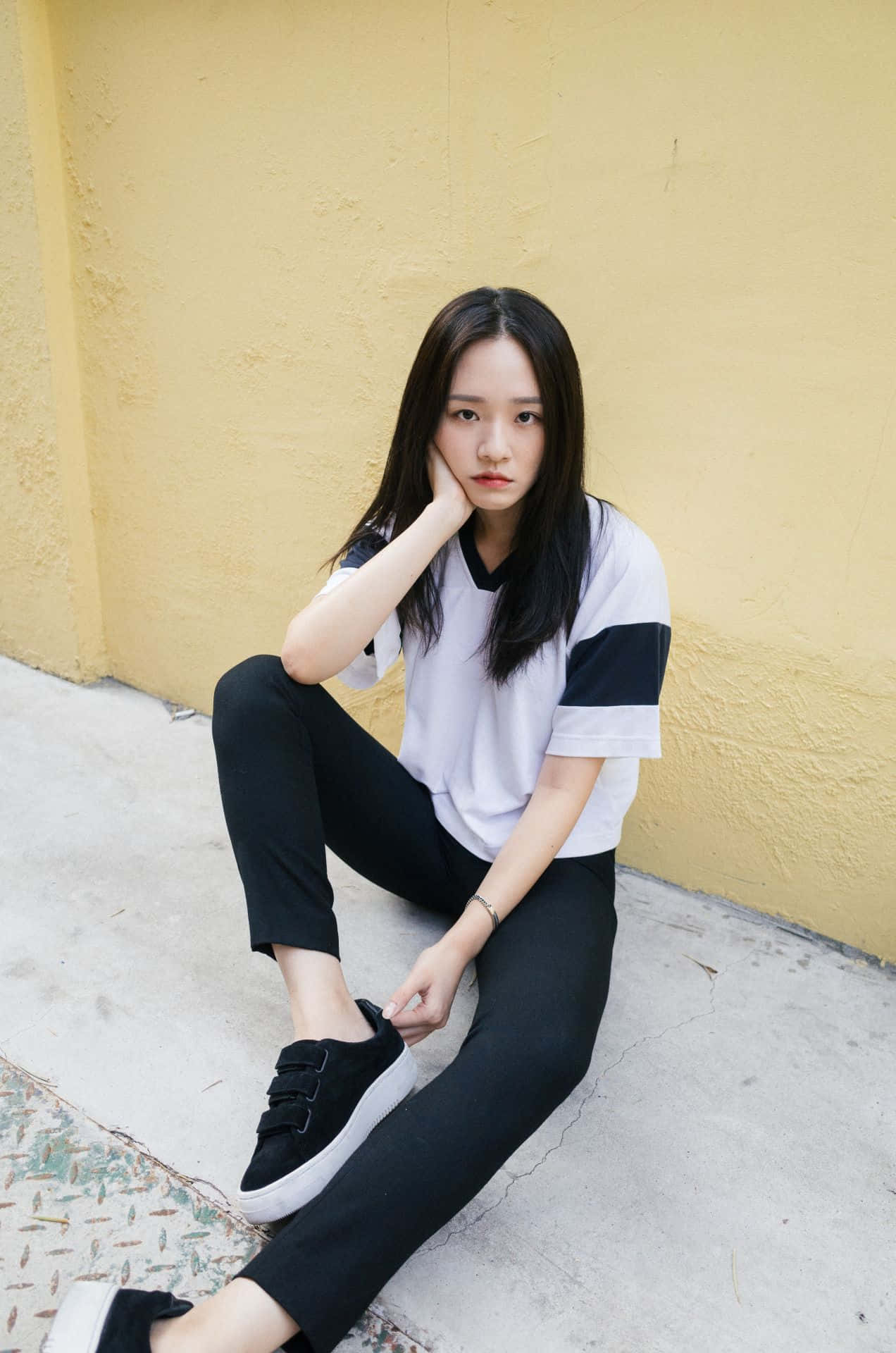 A Young Woman Sitting On The Ground Wearing Black Pants And White T - Shirt Wallpaper