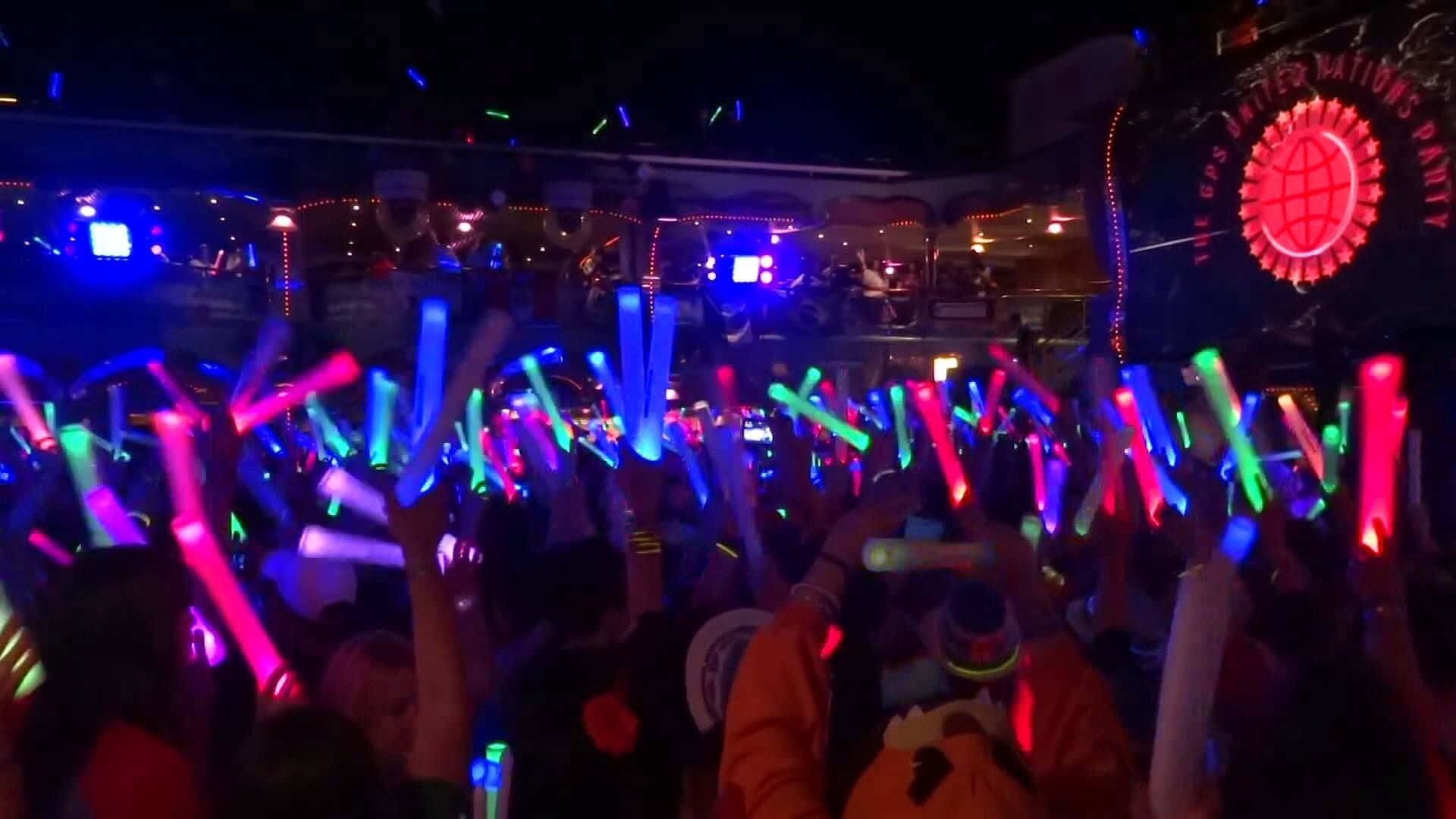 A Crowd Of People Holding Up Glow Sticks At A Nightclub