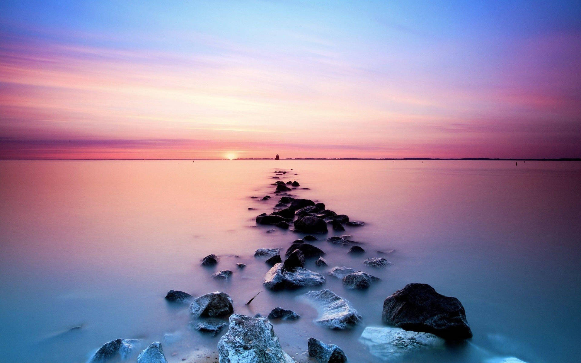 A Rock Line In The Water At Sunset Wallpaper