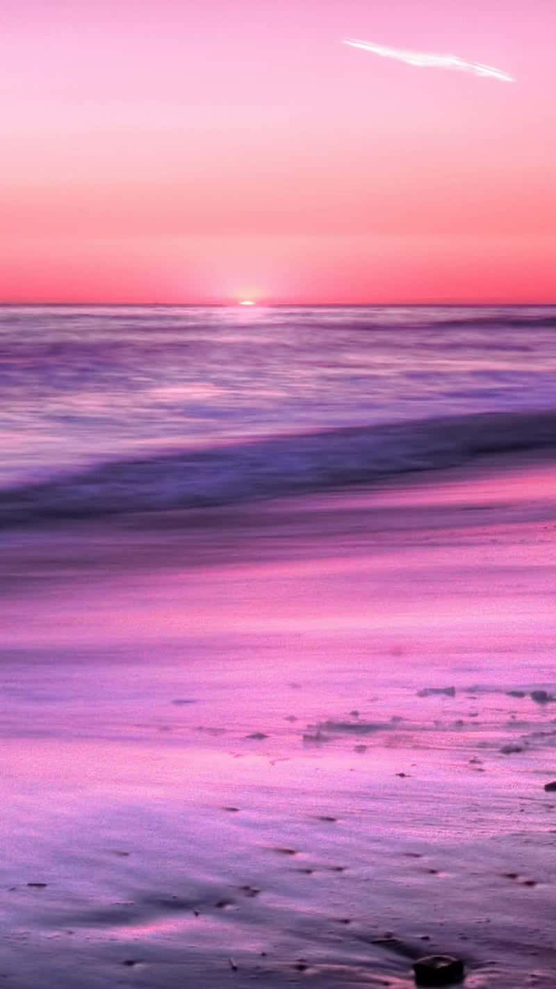 Et pink solnedgang på stranden med bølger, der bryder. Wallpaper