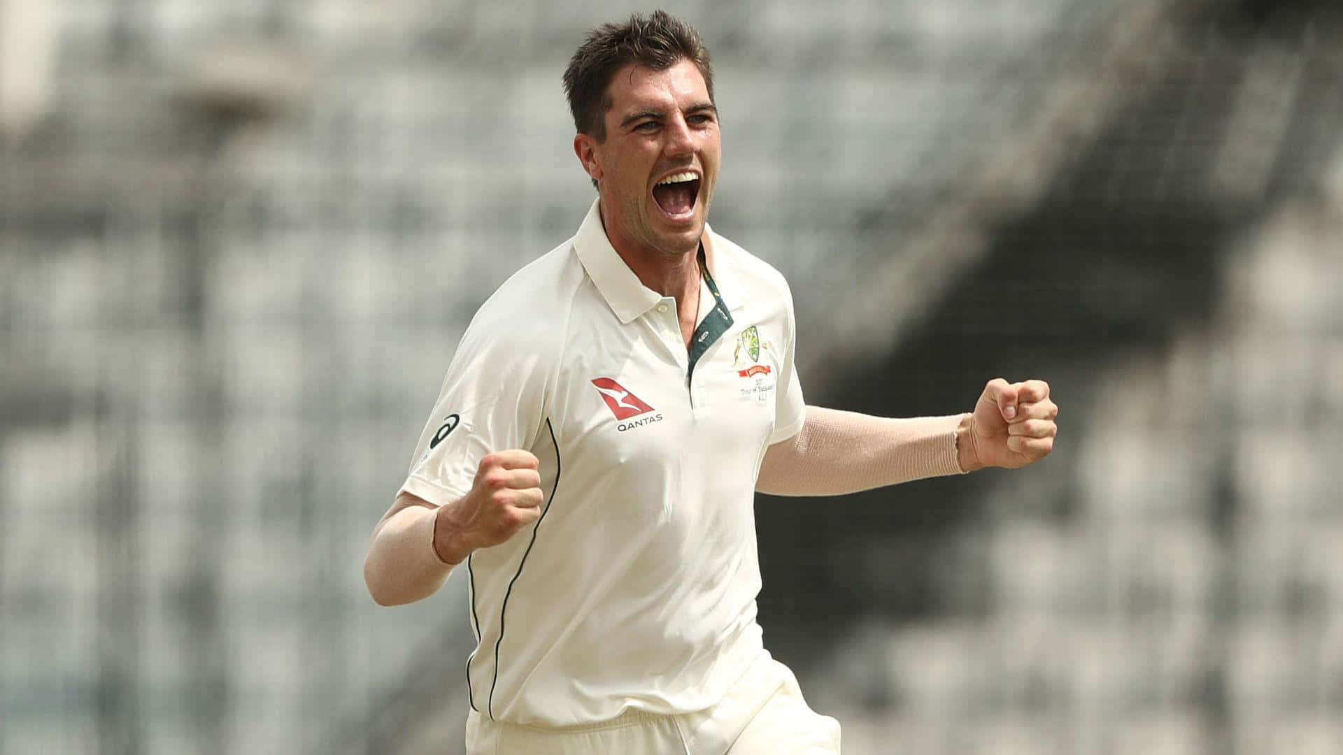 Pat Cummins Wallpaper — A cricket player in white uniform celebrates triumphantly with clenched fists and an open-mouthed yell on a sunlit field.