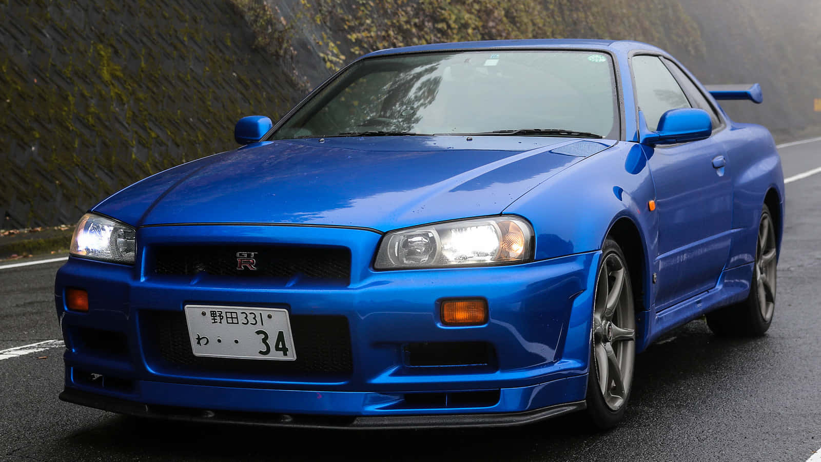 A Blue Sports Car Is Driving Down A Road Wallpaper