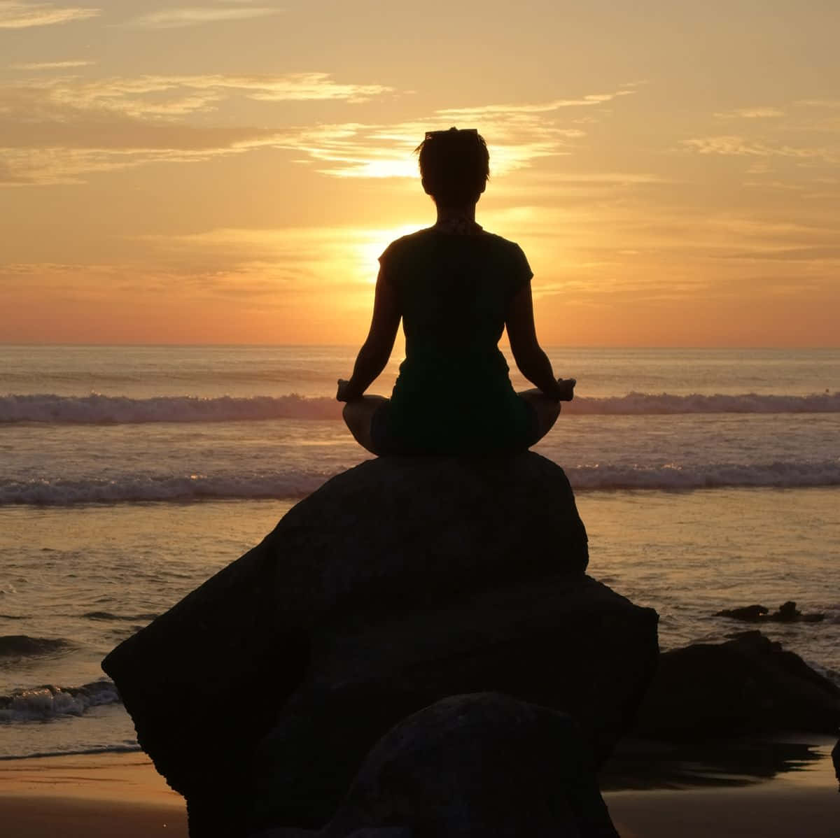 A Woman Is Sitting On Rocks At Sunset