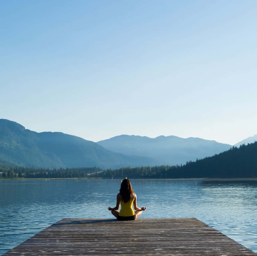 Woman Meditating On A Dock In The Mountains
