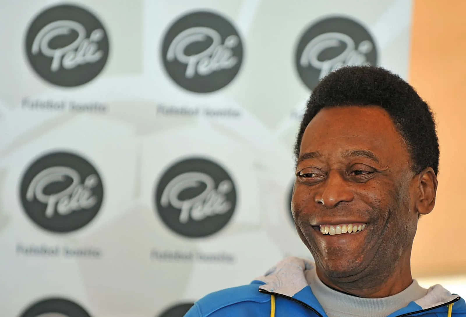 Pele Smiling Against Branded Backdrop Wallpaper