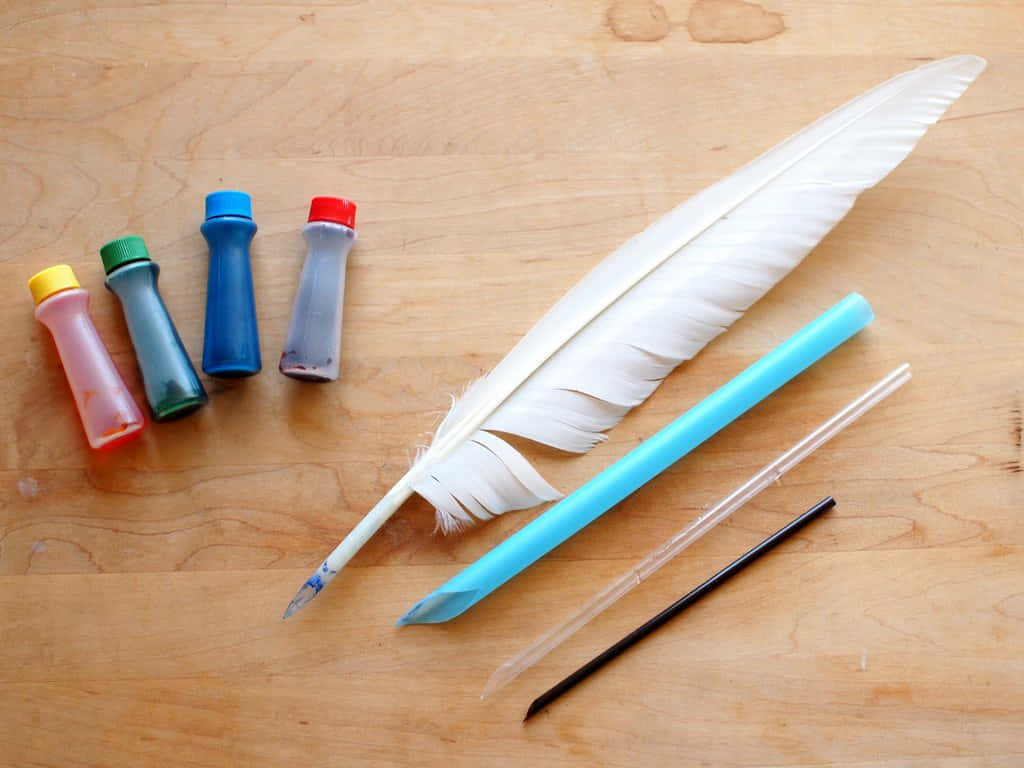 A Feather Pen, Paint, And A Pencil On A Wooden Table