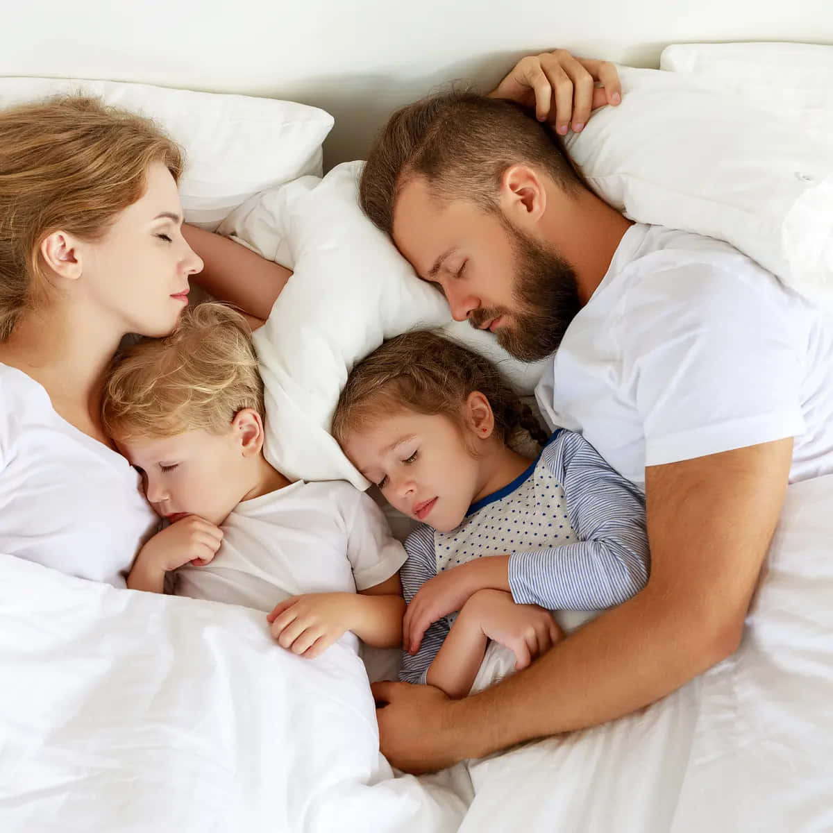 A Family Sleeping In Bed With Two Children