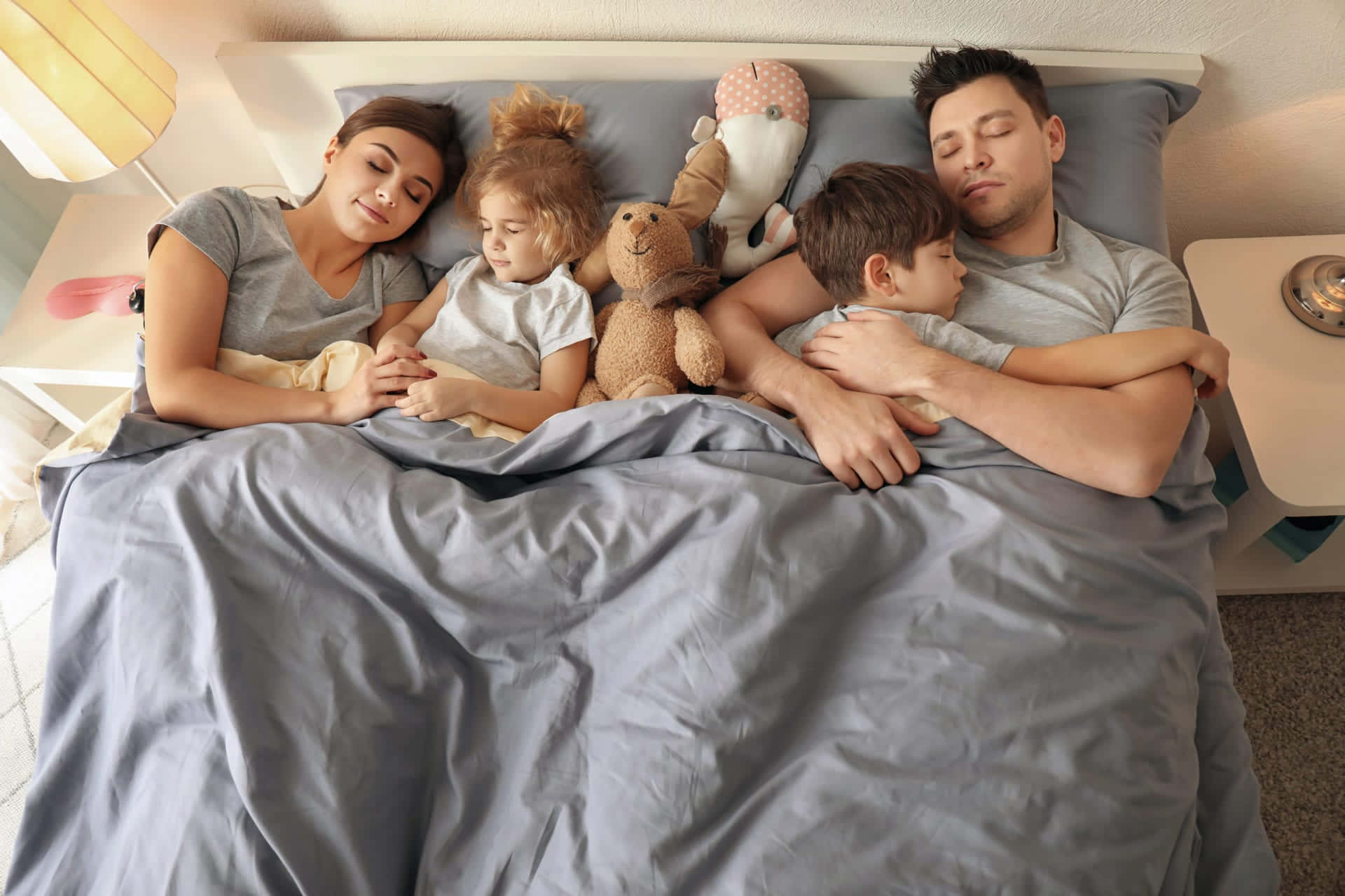 A Family Is Sleeping In Bed With A Teddy Bear