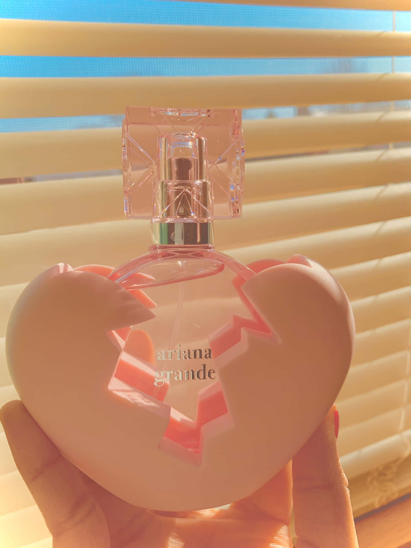 A Person Holding A Pink Perfume Bottle In Front Of A Window