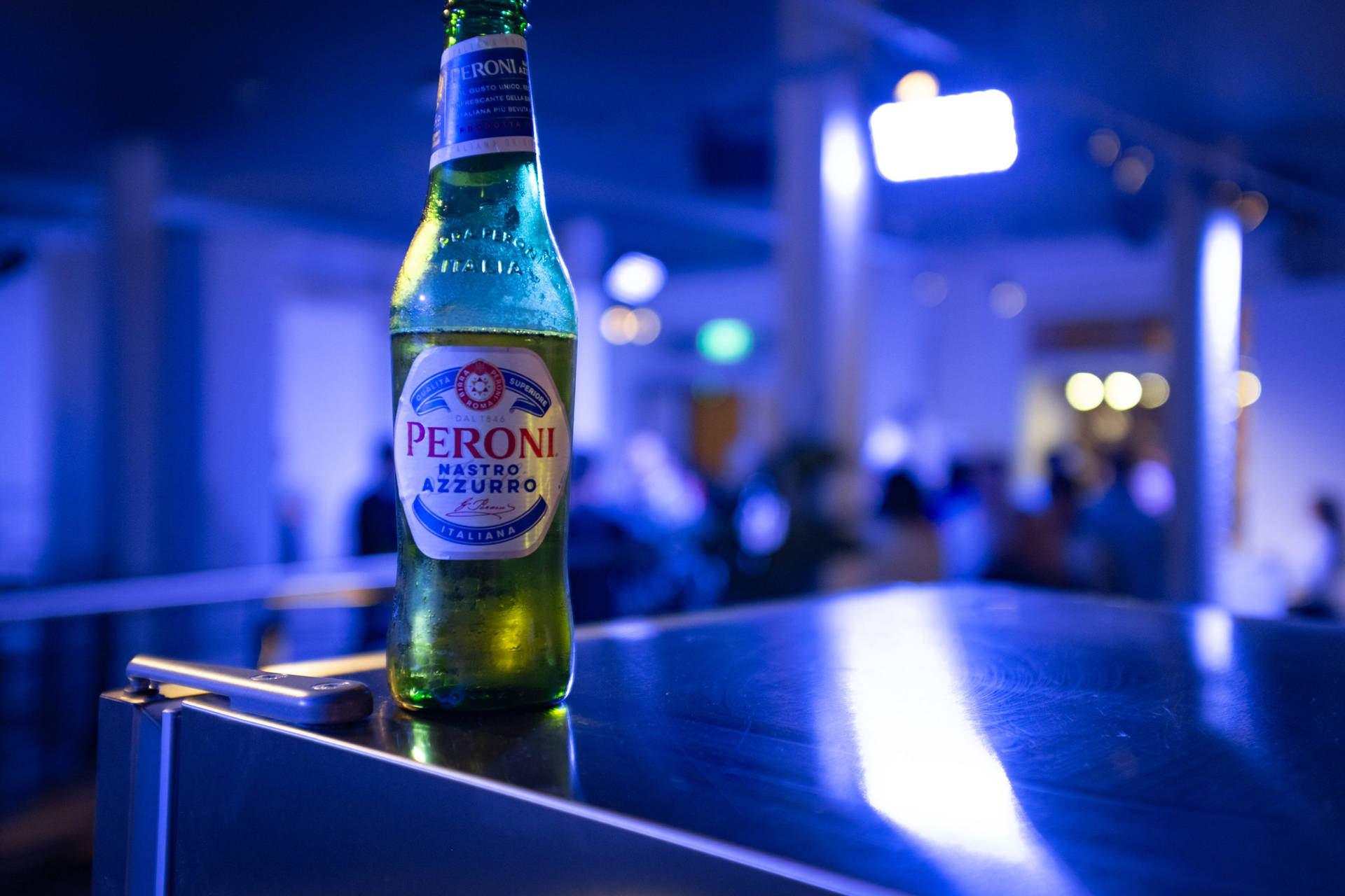 Øl af Peroni i et blåt oplyst rum Wallpaper