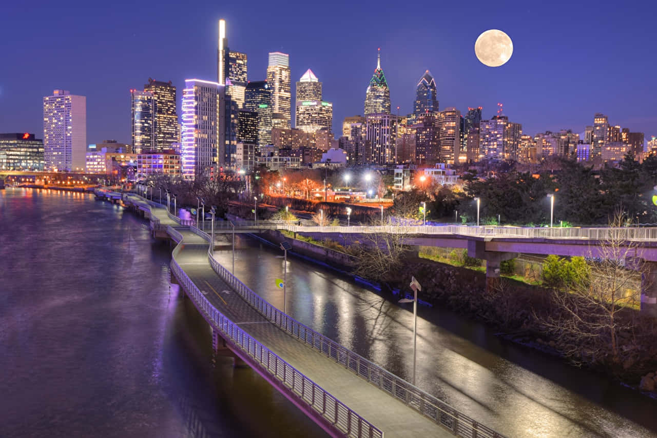 A City Skyline With A Full Moon Over A River Wallpaper