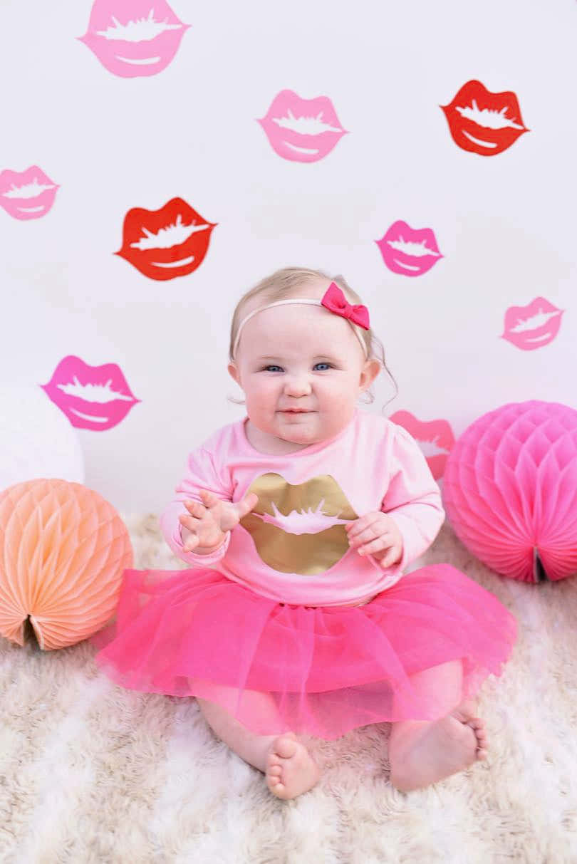 a baby girl in pink sitting in front of a pink wall with lips