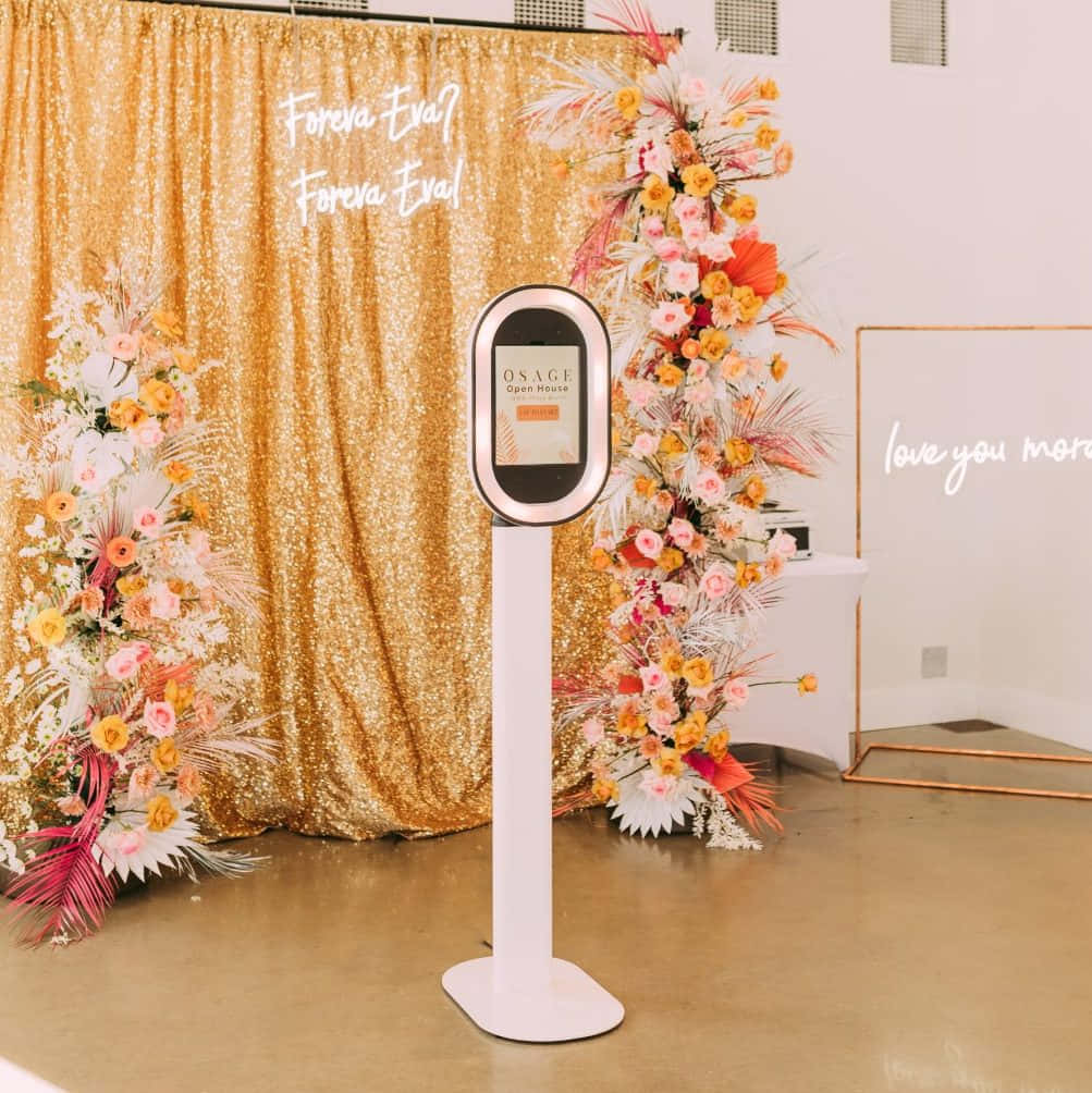 A Photo Booth With Flowers And A Gold Backdrop