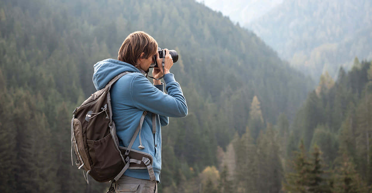 A Man With A Backpack Taking A Picture Of A Forest