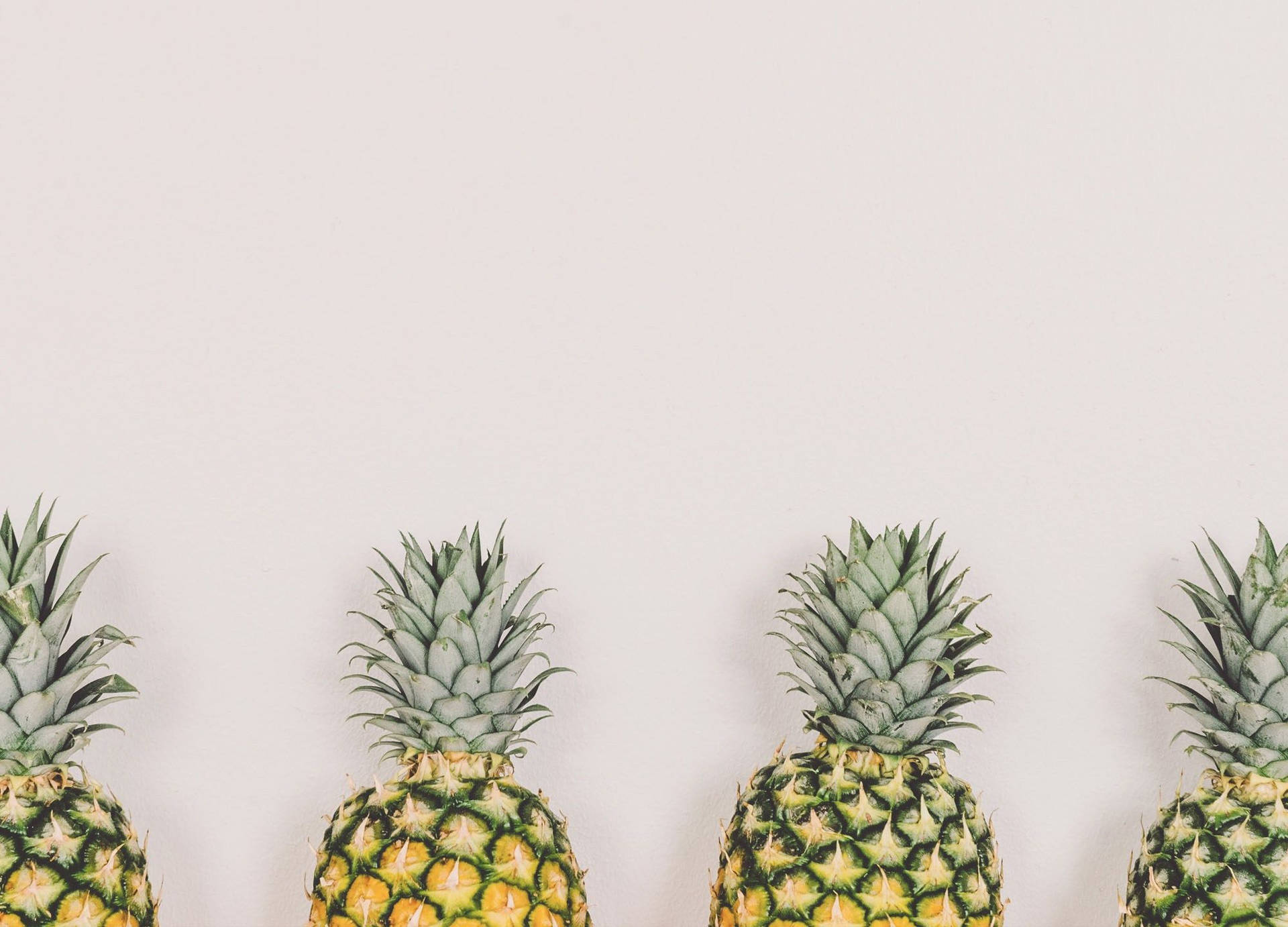An array of pineapples of different sizes, shapes, and colors all lined up side by side. Wallpaper