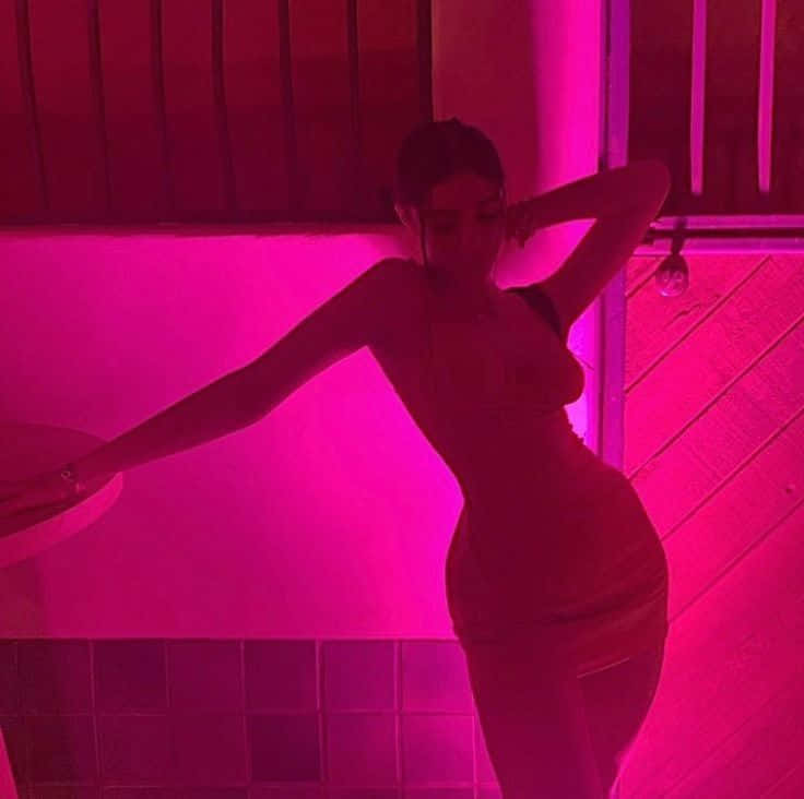 A Woman In A Pink Dress Posing In Front Of A Pink Light Wallpaper