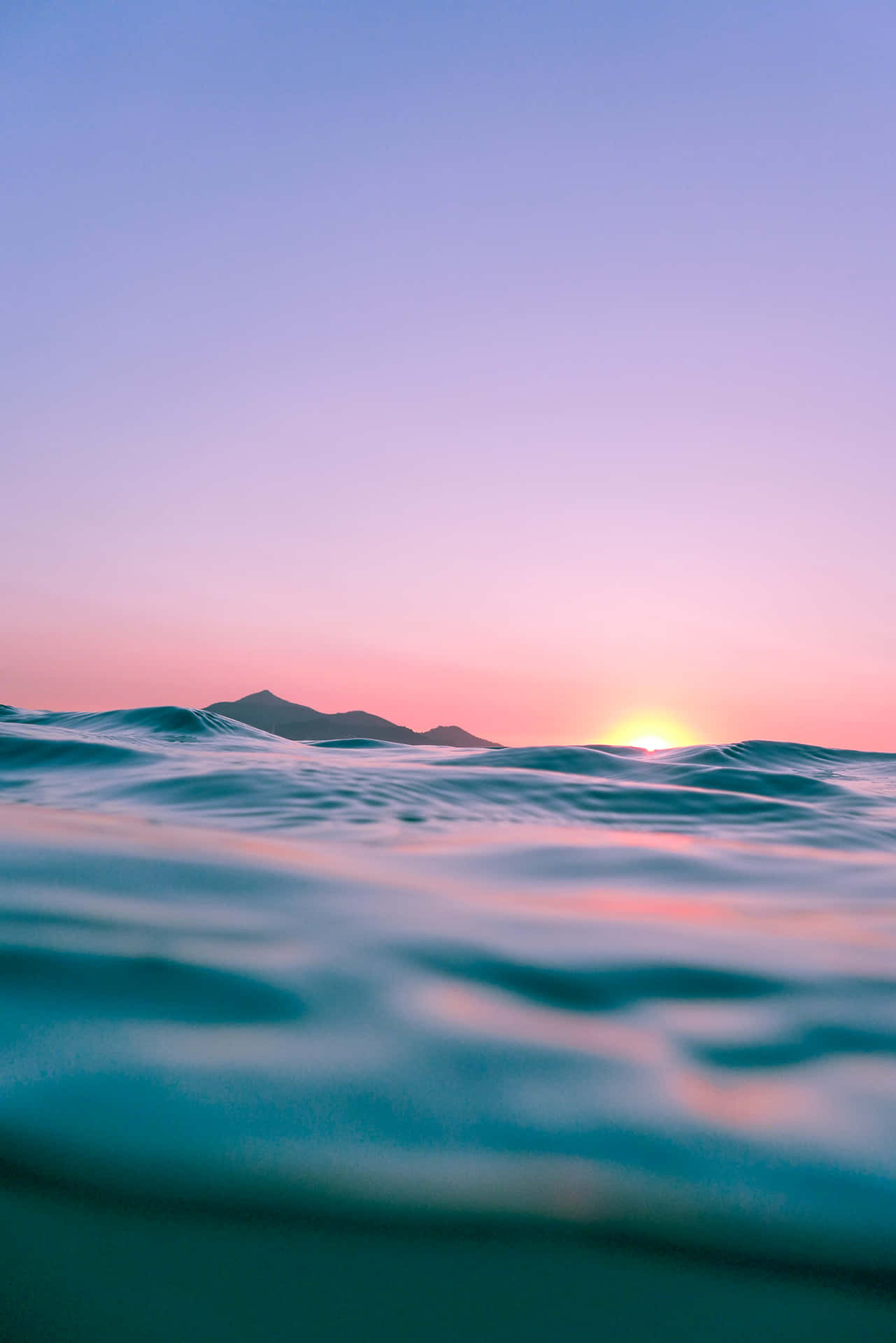 Et solnedgang over havet med bølger og bjerge i det fjerne. Wallpaper