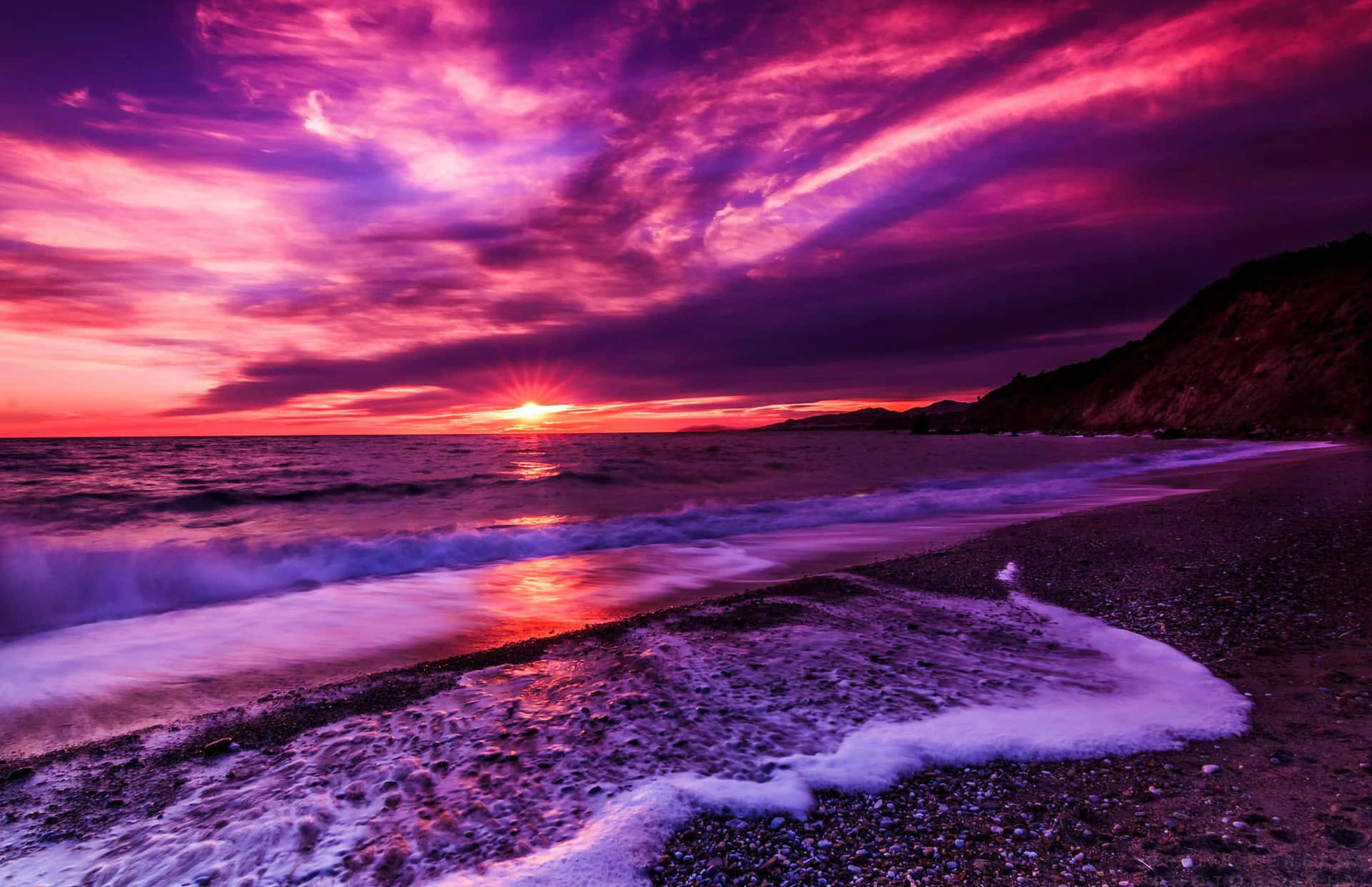 A Purple Sunset Over The Ocean With Waves Wallpaper