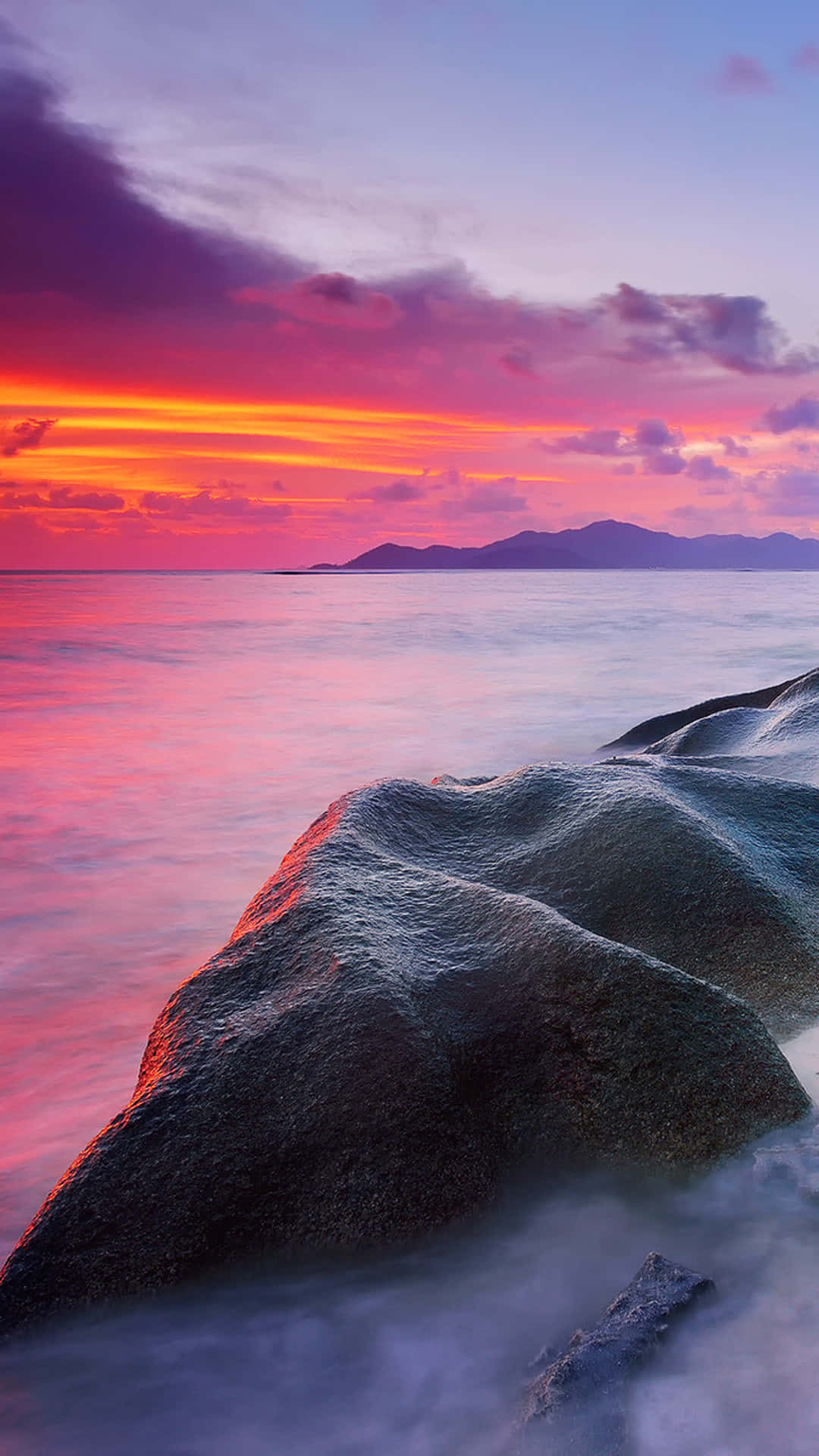 En solnedgang over en strand med sten og vand skyllet langs kysten Wallpaper