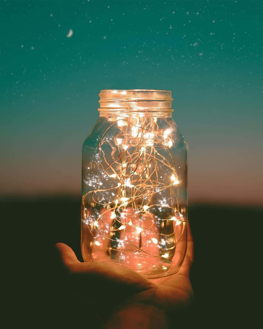 A Hand Holding A Jar Of Fairy Lights Wallpaper