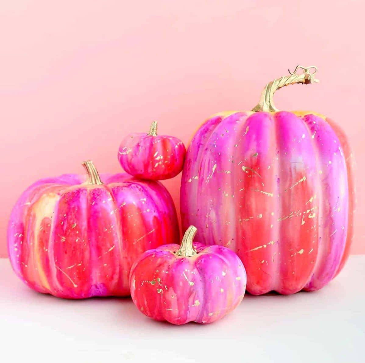 Three Pink And Gold Painted Pumpkins On A Pink Background Wallpaper