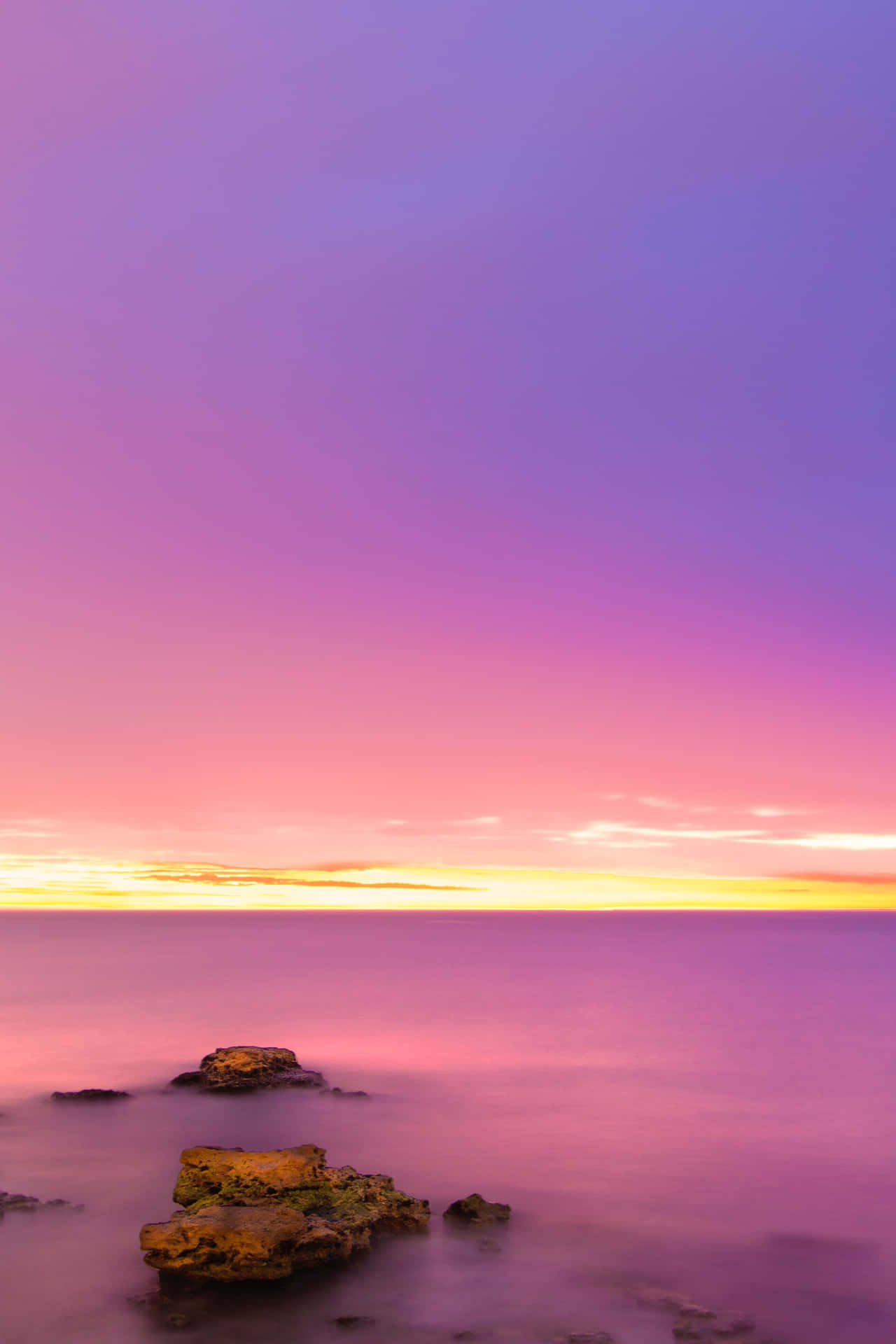 A Purple Sunset Over Rocks And Water