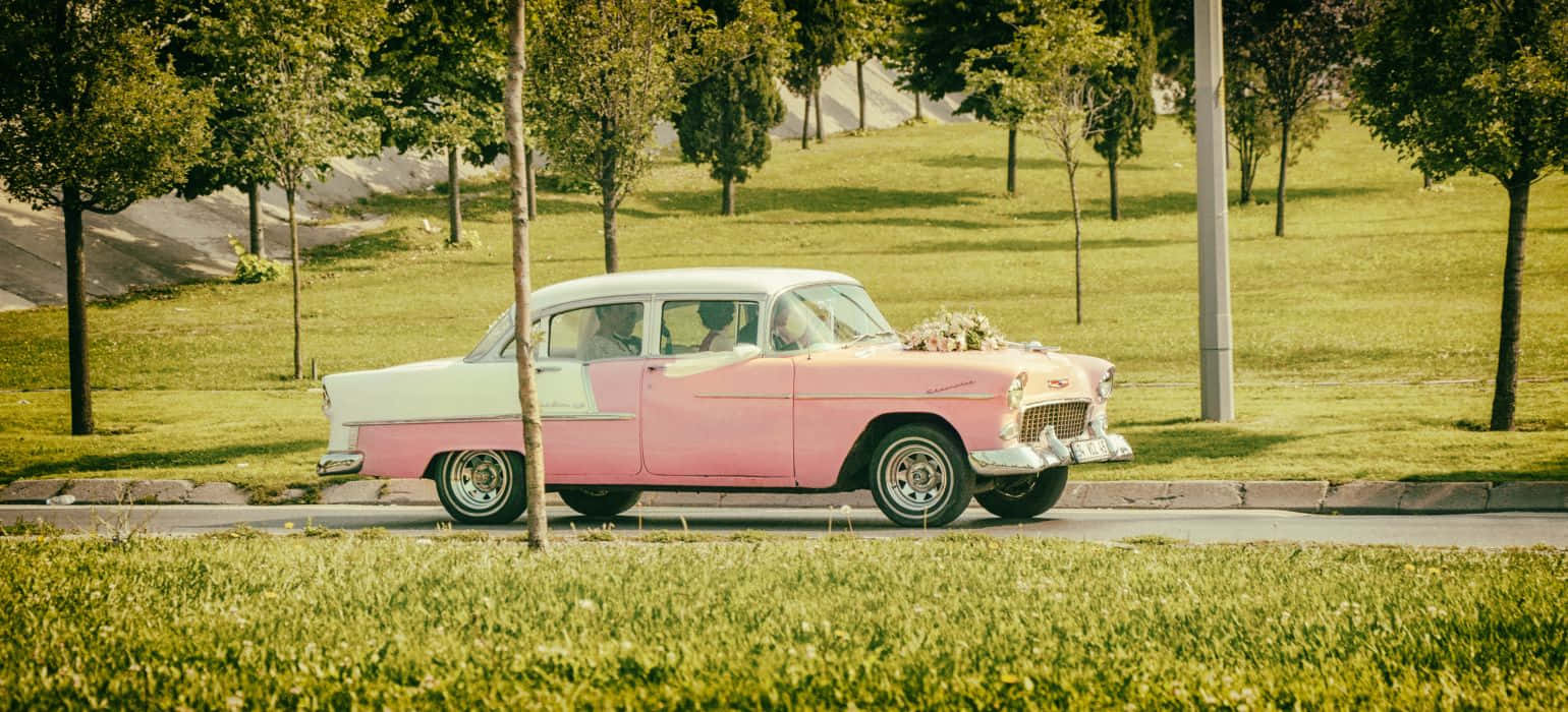 An eye-catching pink vintage car parked on a cobblestone street Wallpaper