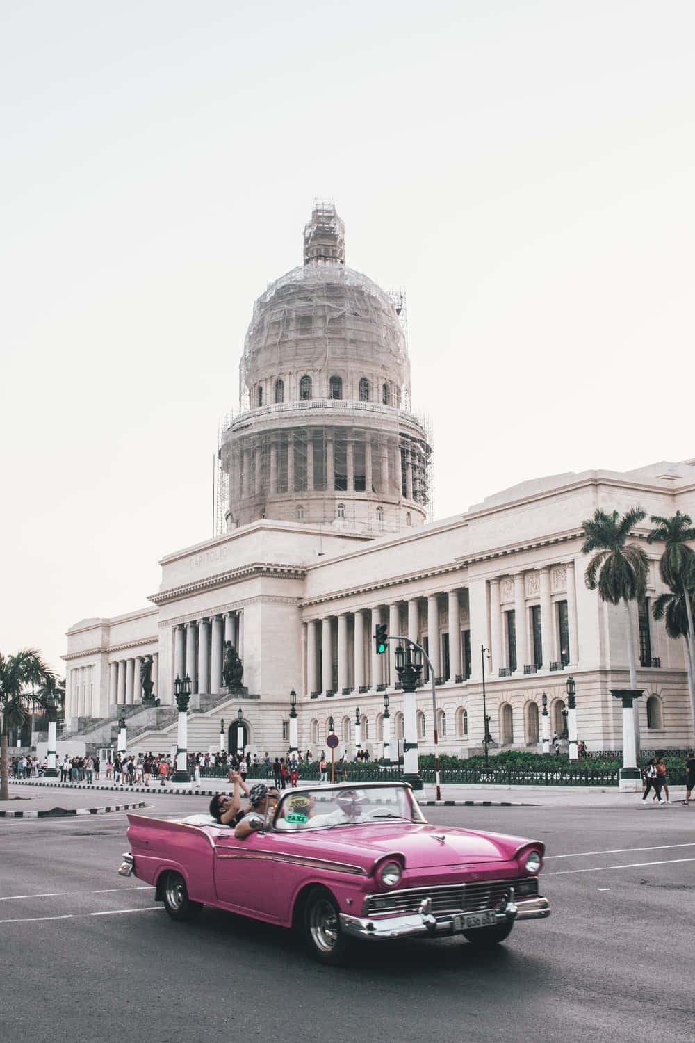 En lyserød cabriolet kører ned ad gaden foran et bygning med efeu vokser op ad væggene. Wallpaper