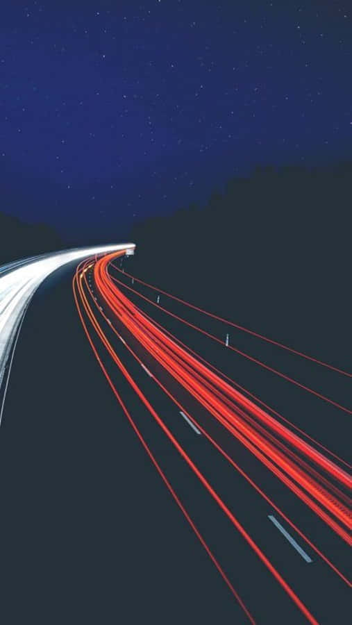 A Nighttime Image Of A Highway With Cars Driving On It