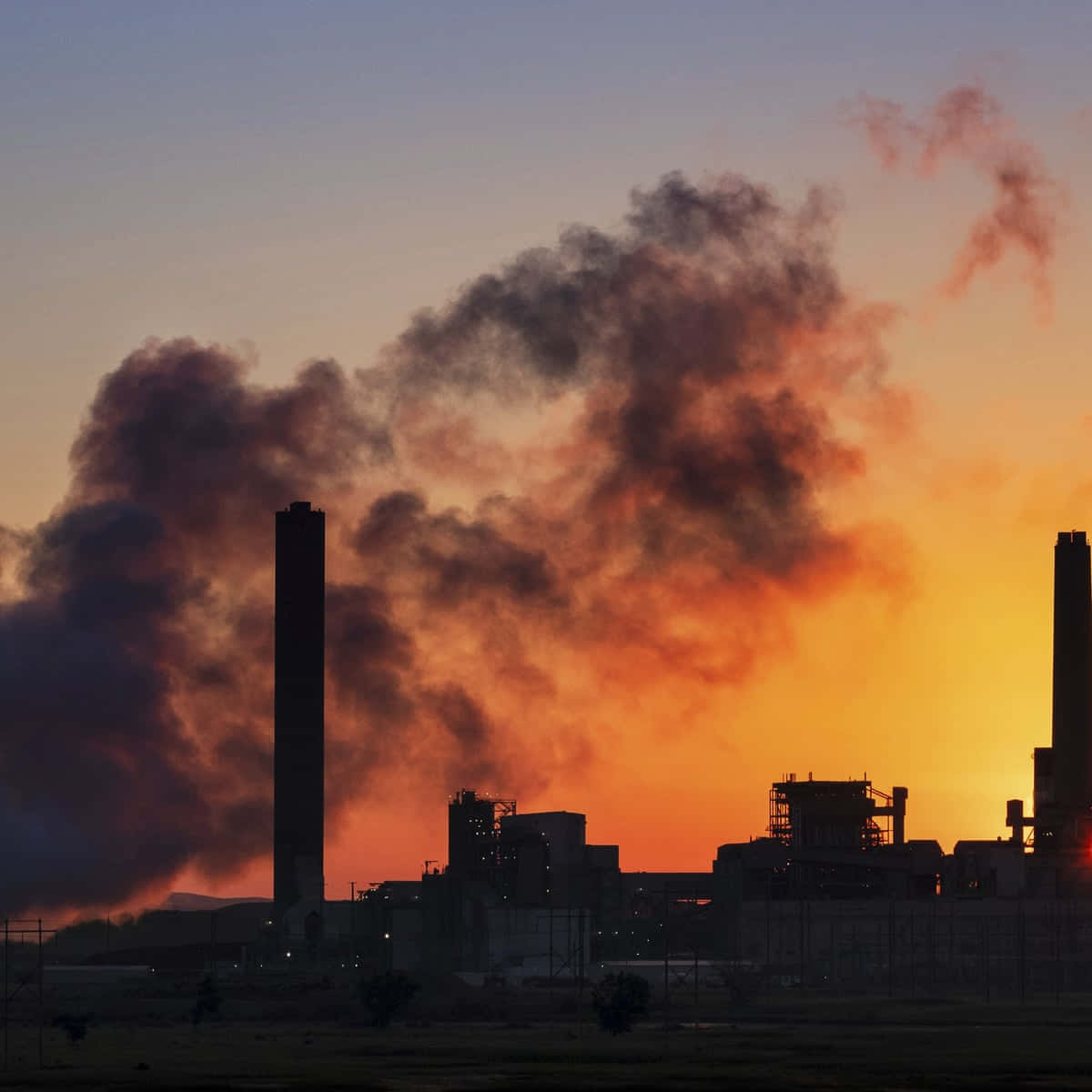 A Factory With Smoke Coming Out Of It At Sunset