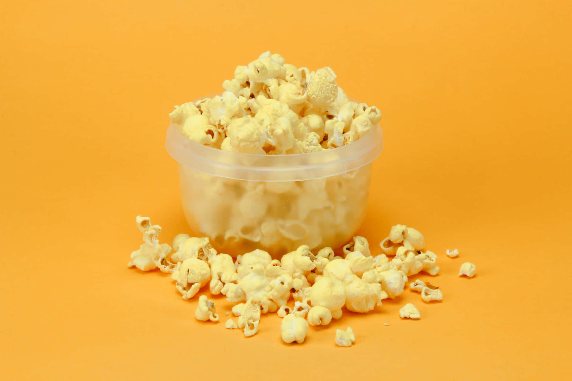 A White Plastic Container With Popcorn On An Orange Background