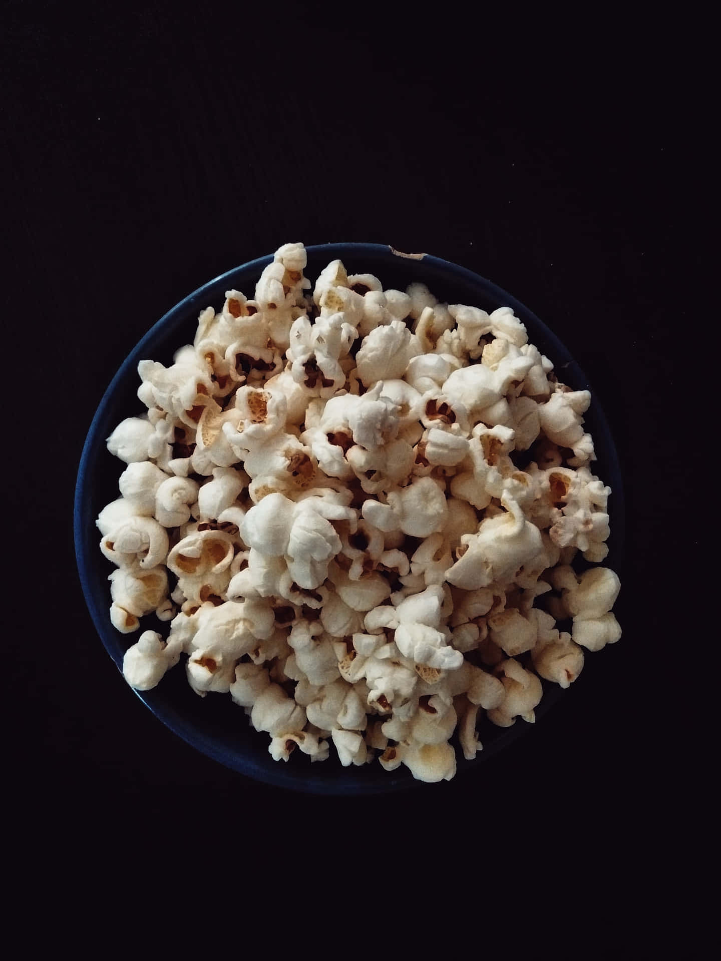 A Bowl Of Popcorn On A Black Table