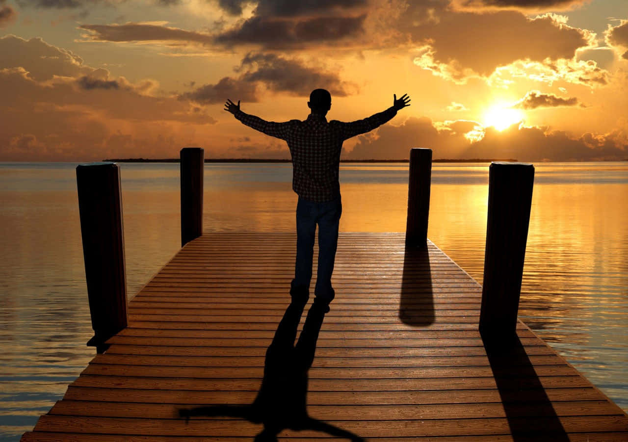 Man Standing On A Dock At Sunset