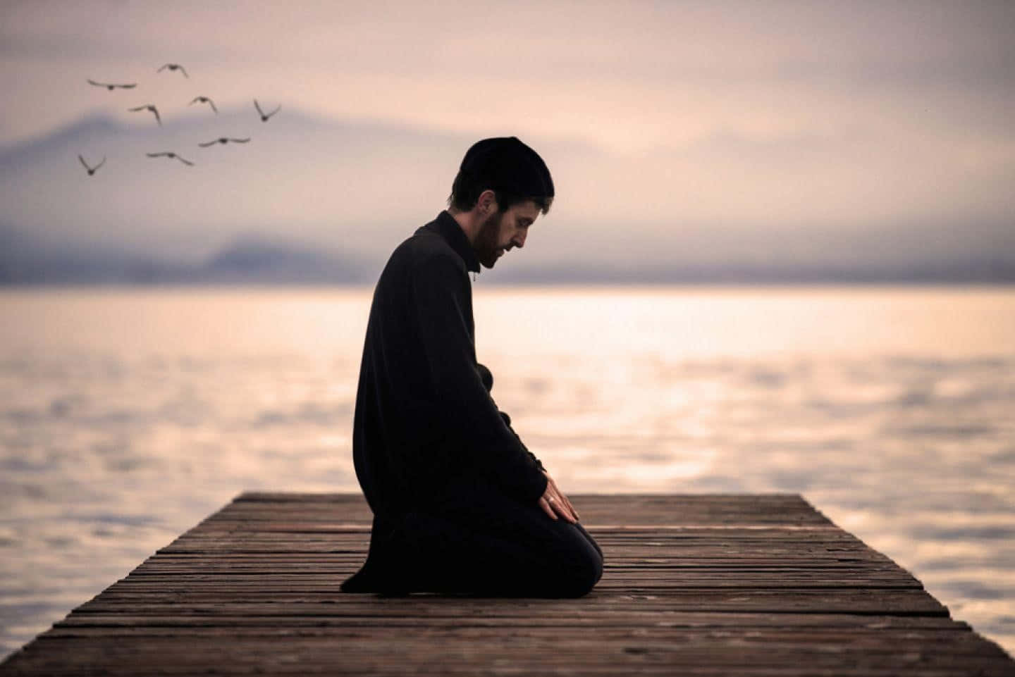 A person in deep prayer with hands clasped in front of a serene nature backdrop