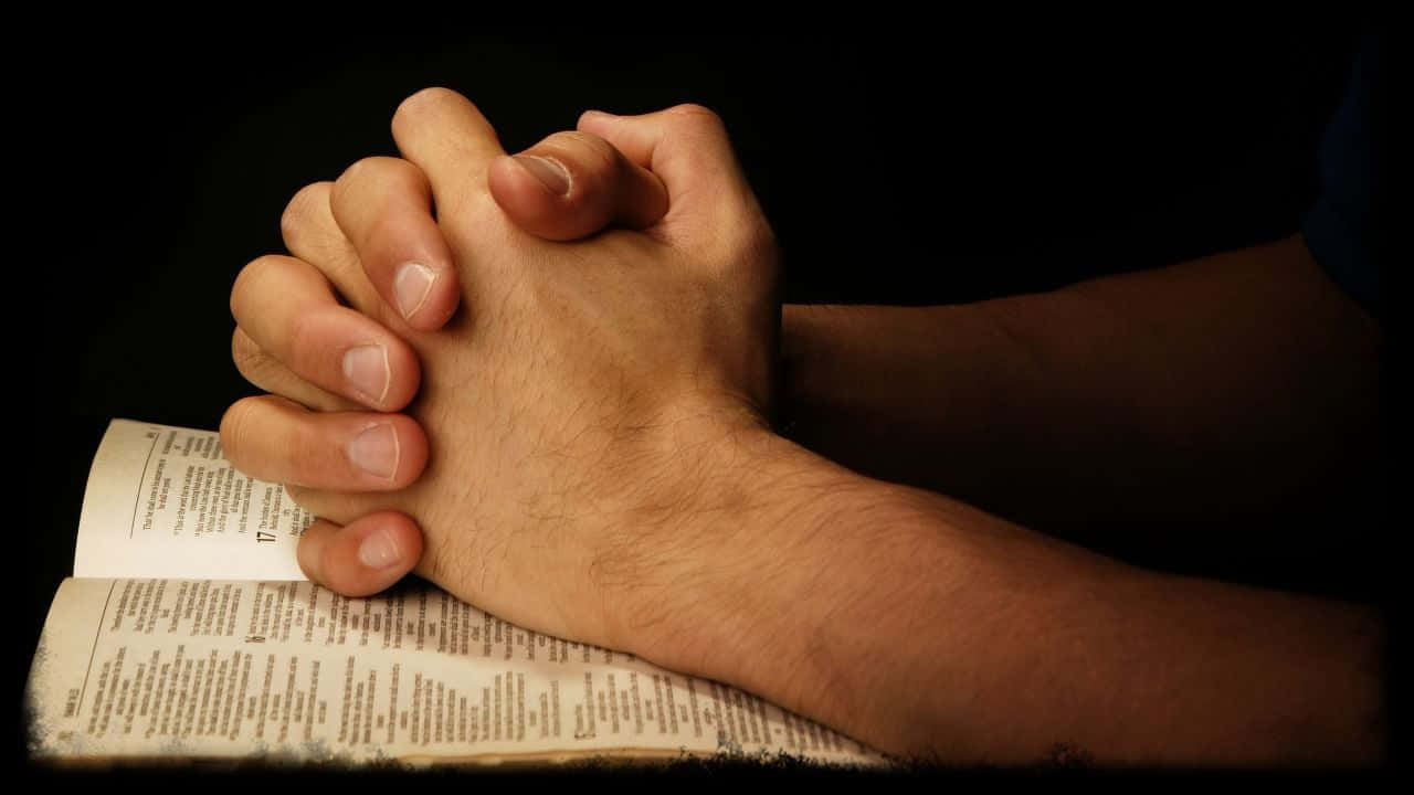 a person's hands are praying on a bible Wallpaper