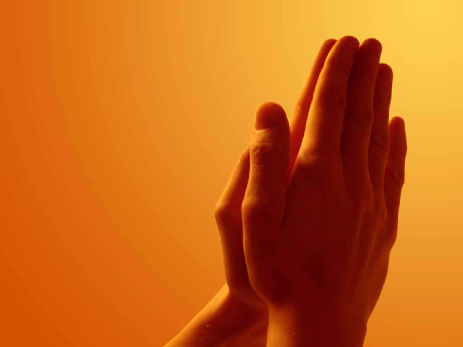 A Woman's Hands Are Clasped In Prayer Against An Orange Background