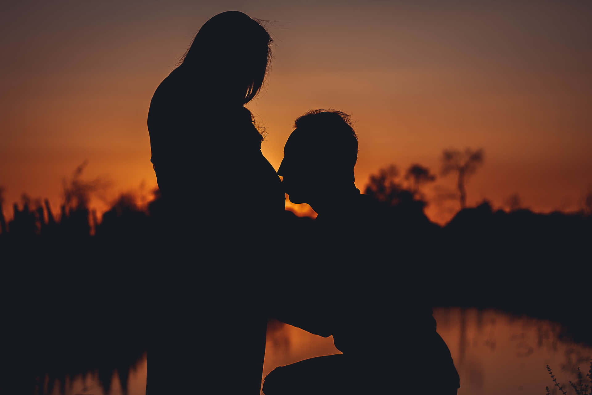 Pregnant Couple Kissing Baby Bump Sunset Silhouette Wallpaper