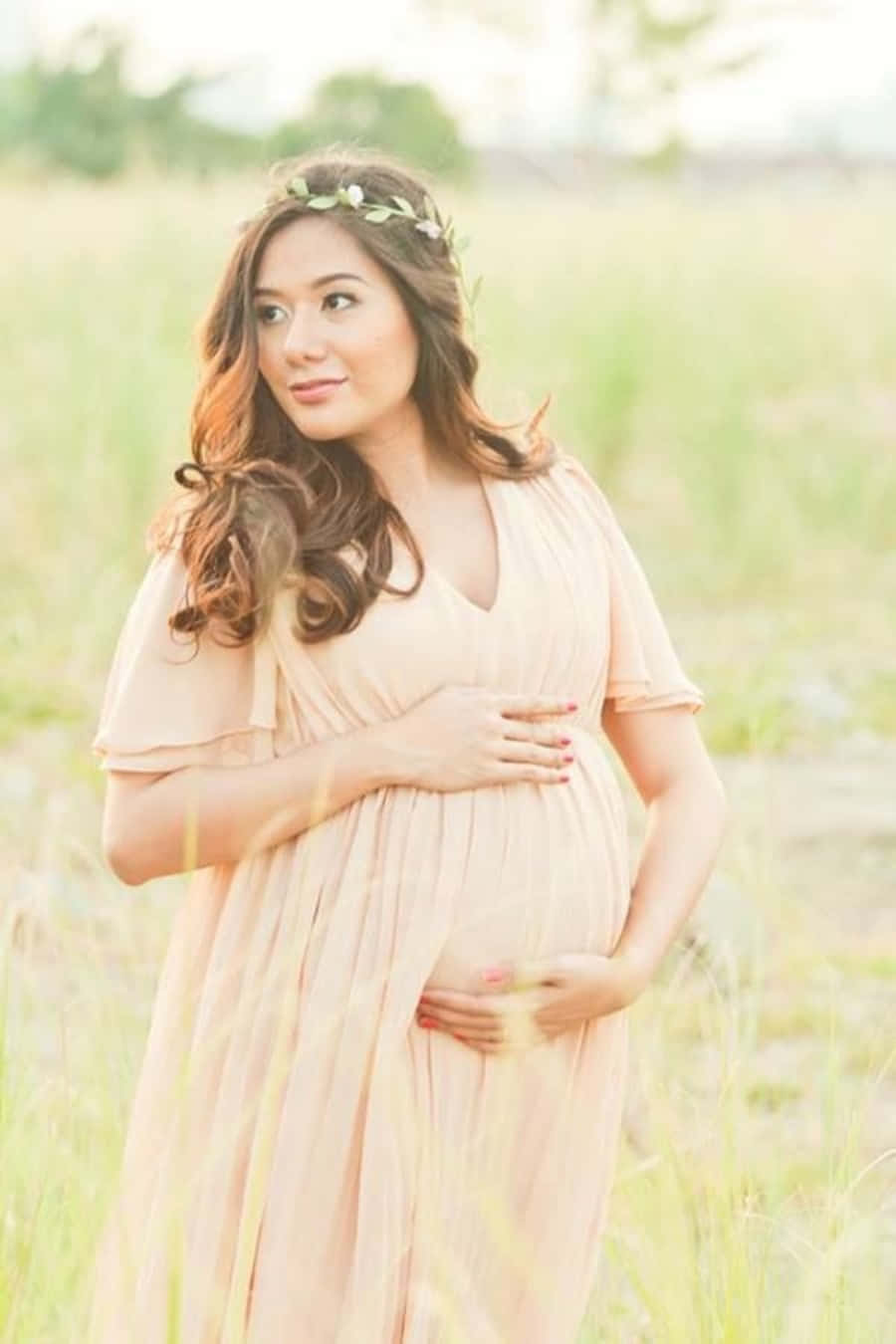 A Pregnant Woman In A Pink Dress Standing In A Field