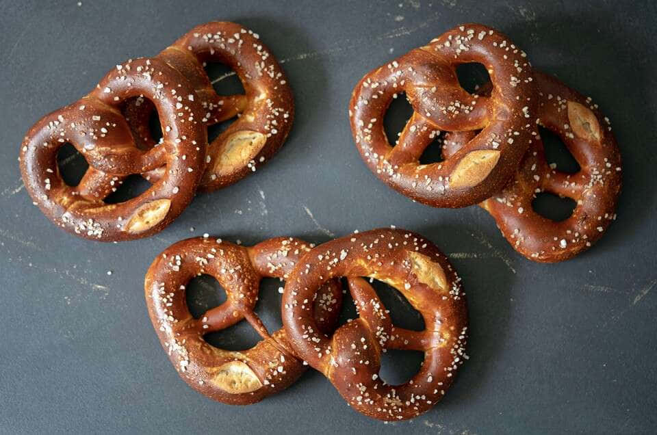 Four Pretzels With Salt And Pepper On A Dark Surface