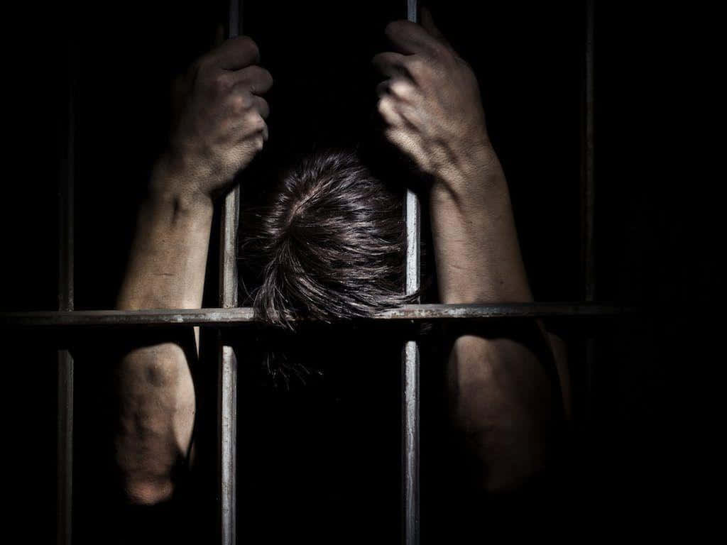 A Man Is Holding His Head Up In A Jail Cell