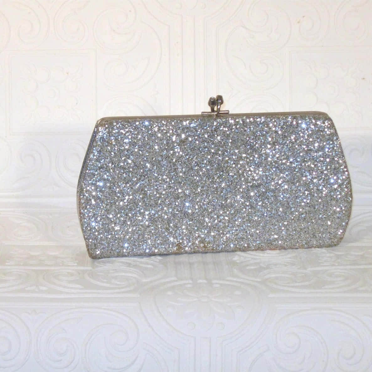 A Silver Glitter Clutch Bag On A White Table