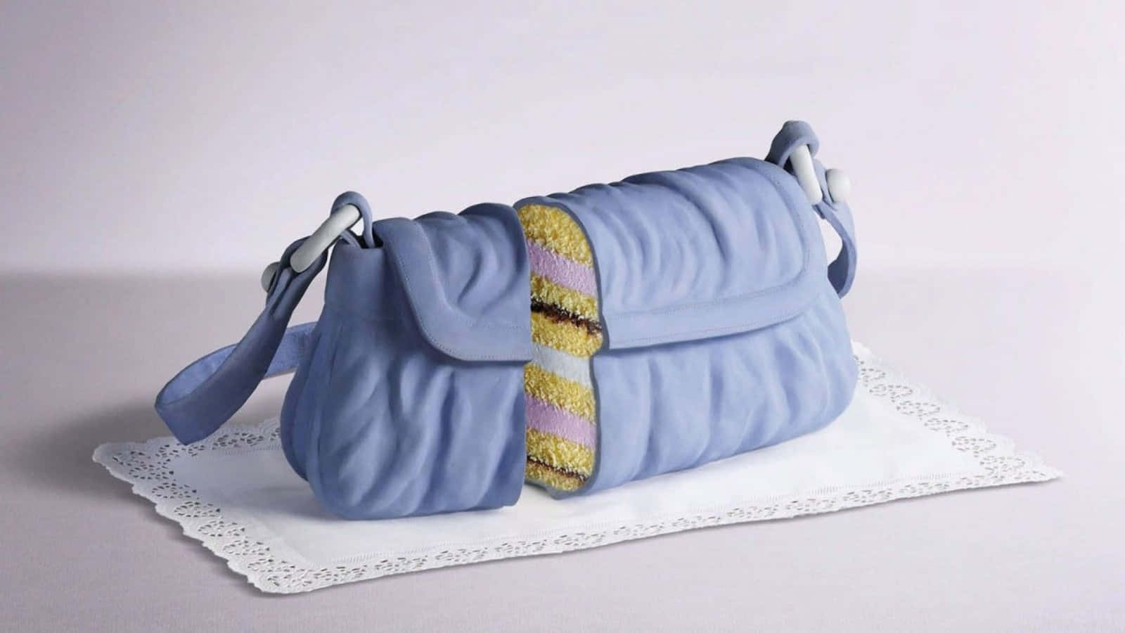 A Blue Purse Cake On A White Tablecloth