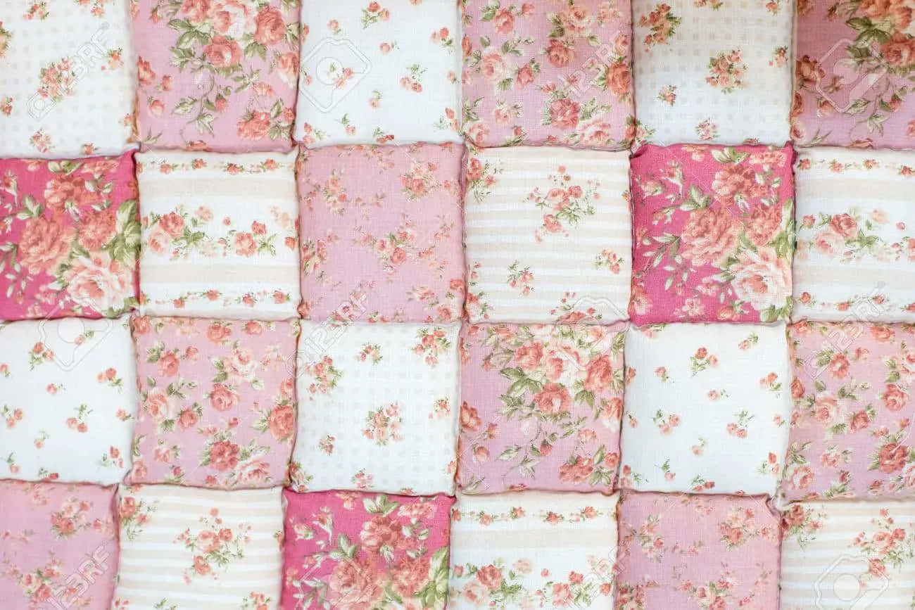 a pink and white quilt with floral patterns Wallpaper