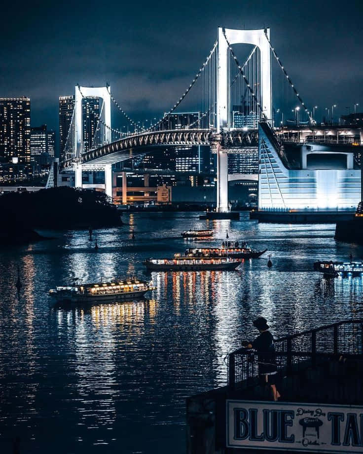 A Bridge With Boats And Lights In The Background