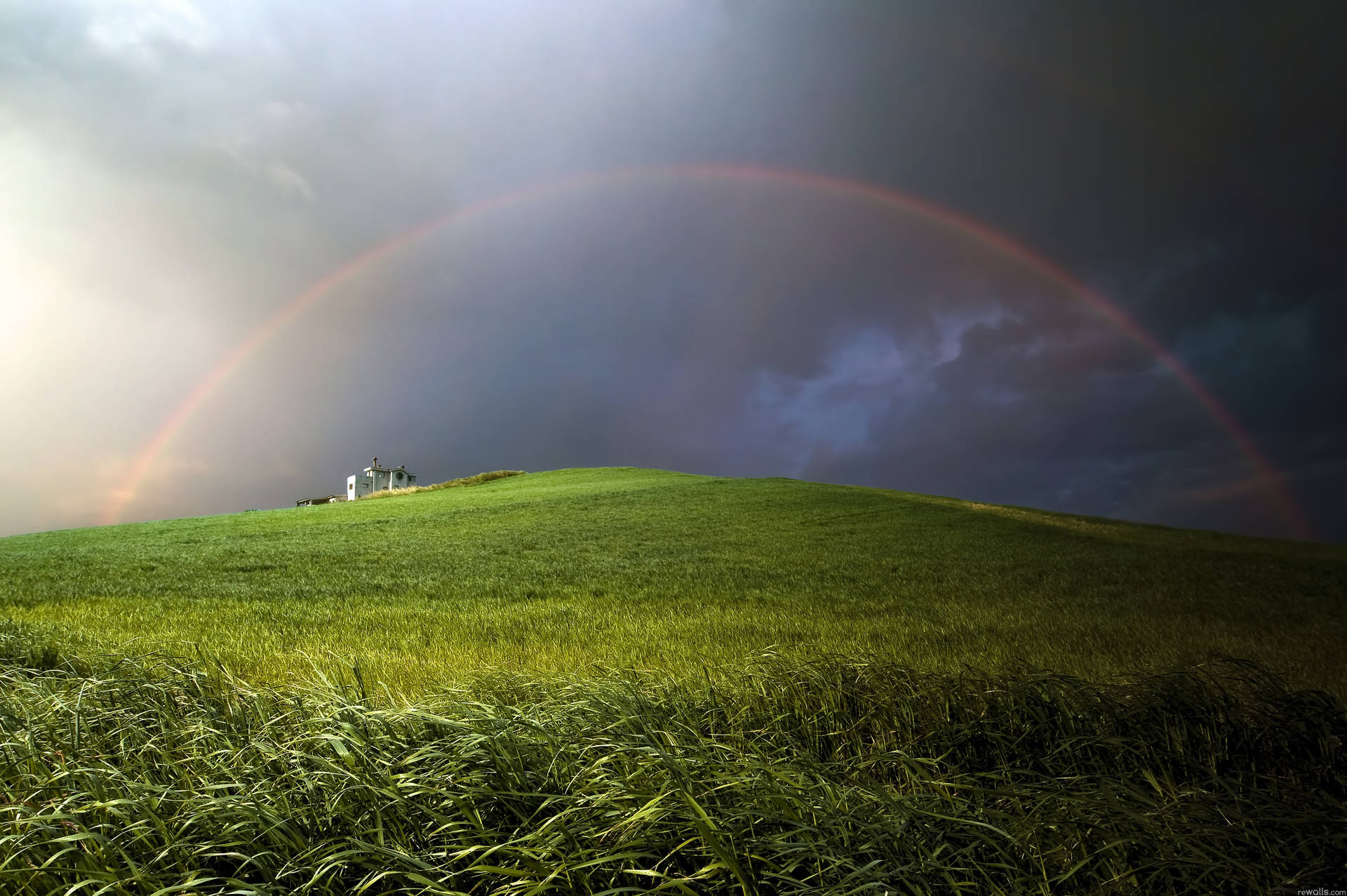 Standing at the peak of the hills with a beautiful rainbow in sight Wallpaper