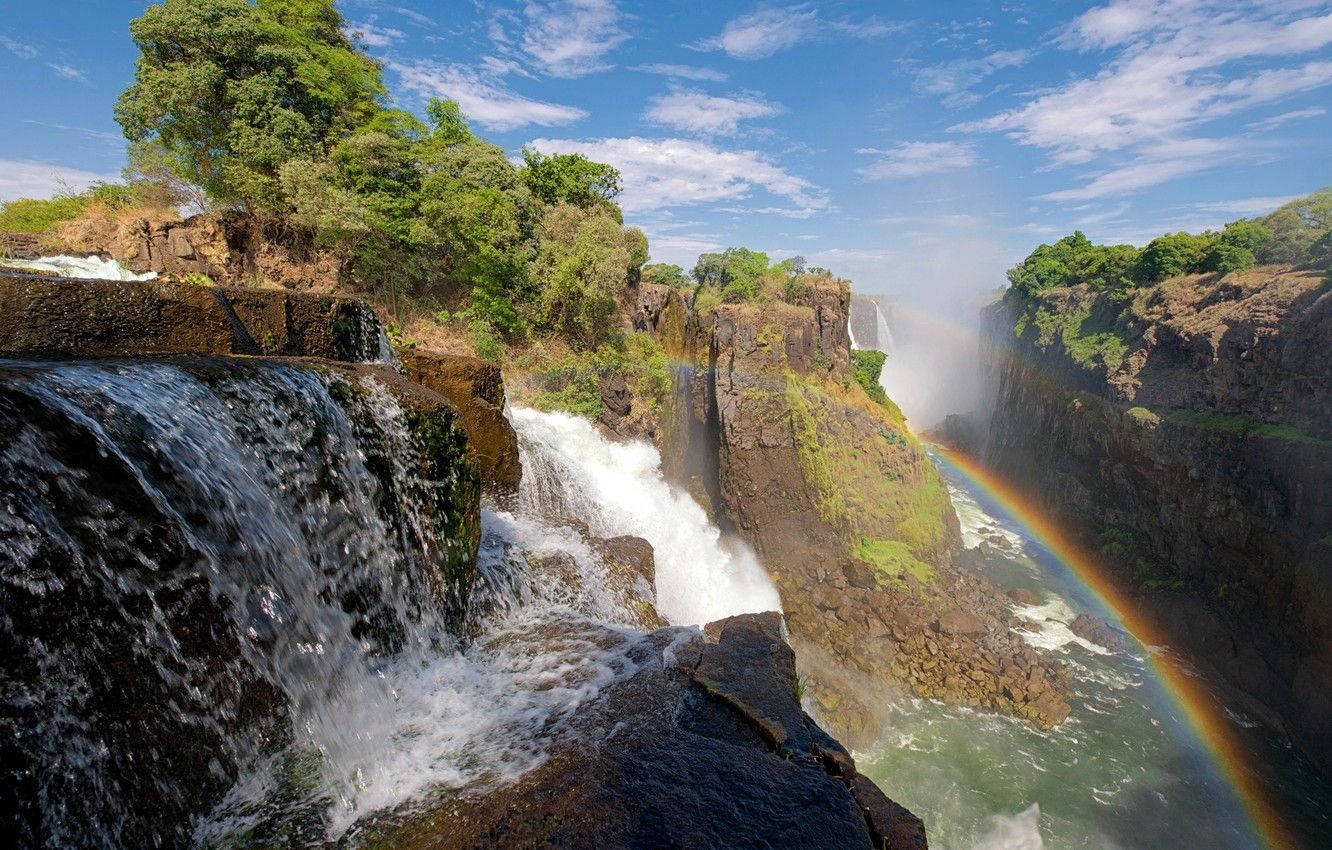 Rainbow Over A Falls In Zimbabwe Background