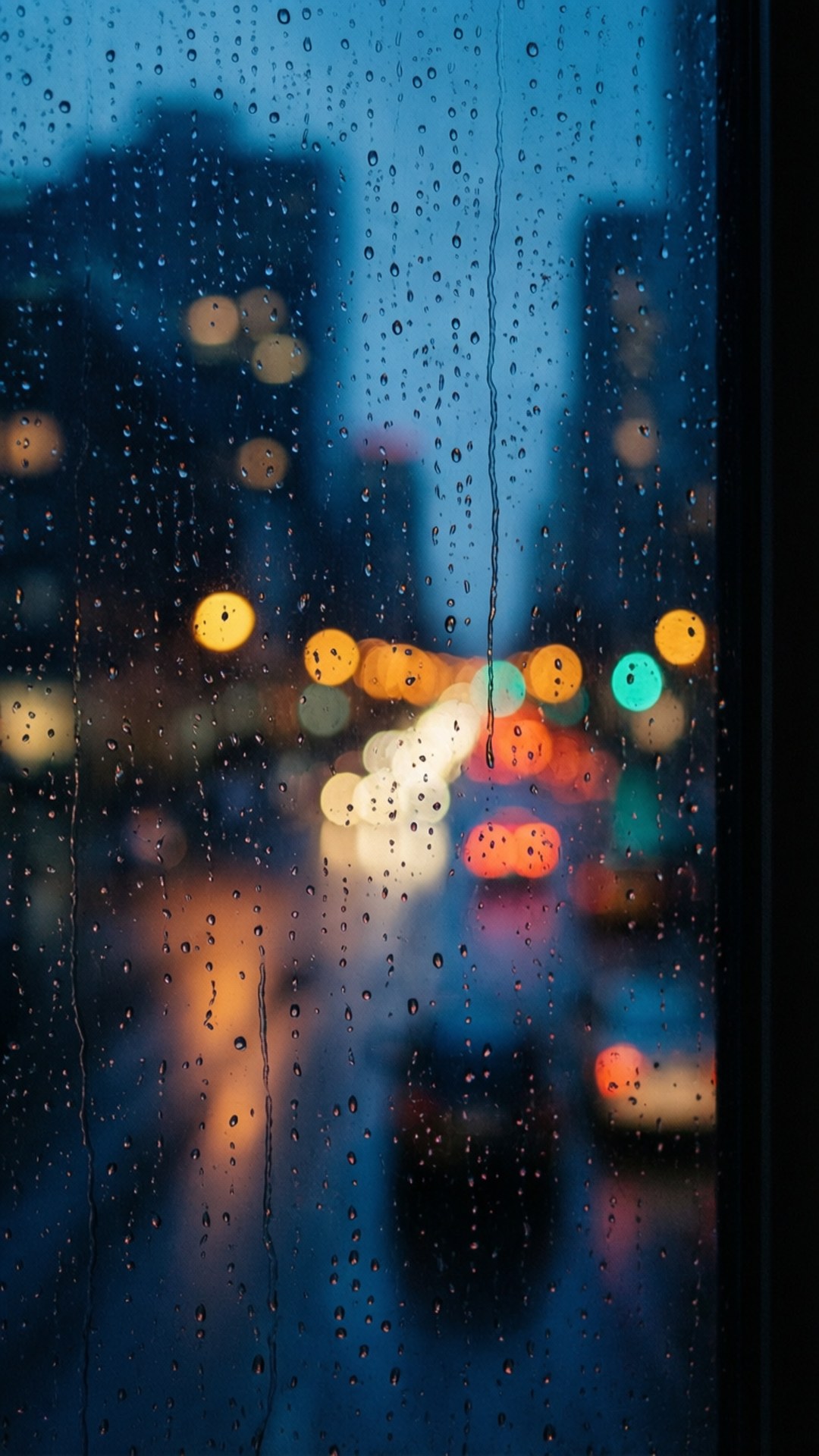 Regndråper på glass med bokeh bylys i bakgrunnen.