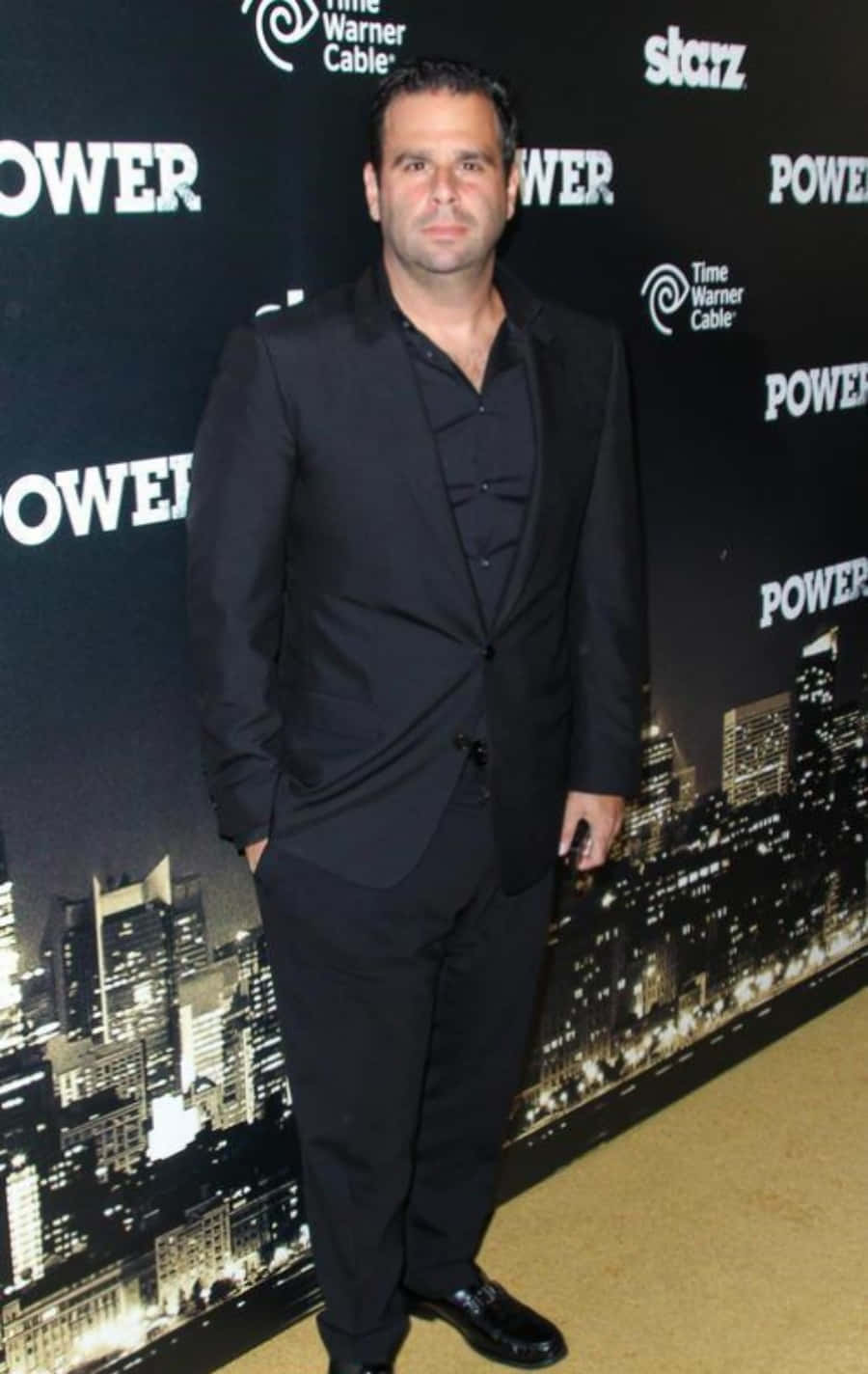 A Man In A Black Suit Standing On A Carpet