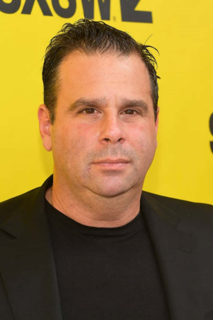 A Man In A Black Shirt Standing In Front Of A Yellow Wall