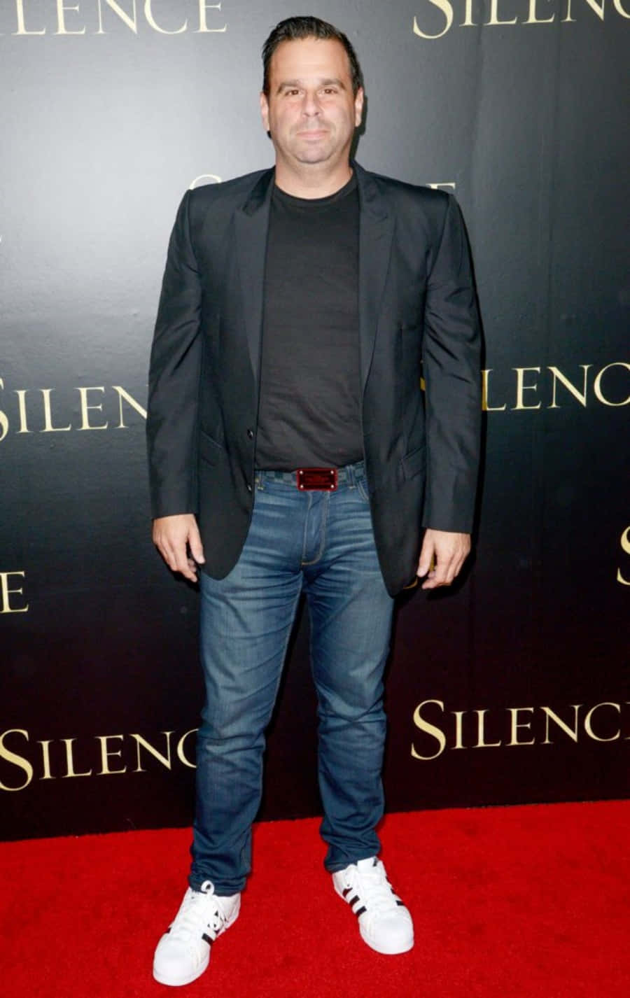 En mand i jeans og jakke står på et rødt gulv.